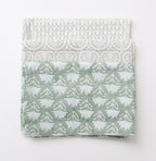 Drie theedoeken met verschillende prints in licht groen en zacht grijs liggen opgevouwen op elkaar. De bovenste heeft een print met bloemen, de middelste een print geïnspireerd op schelpen en de onderste een subtiele geometrisch print genaamd Little Crown. 