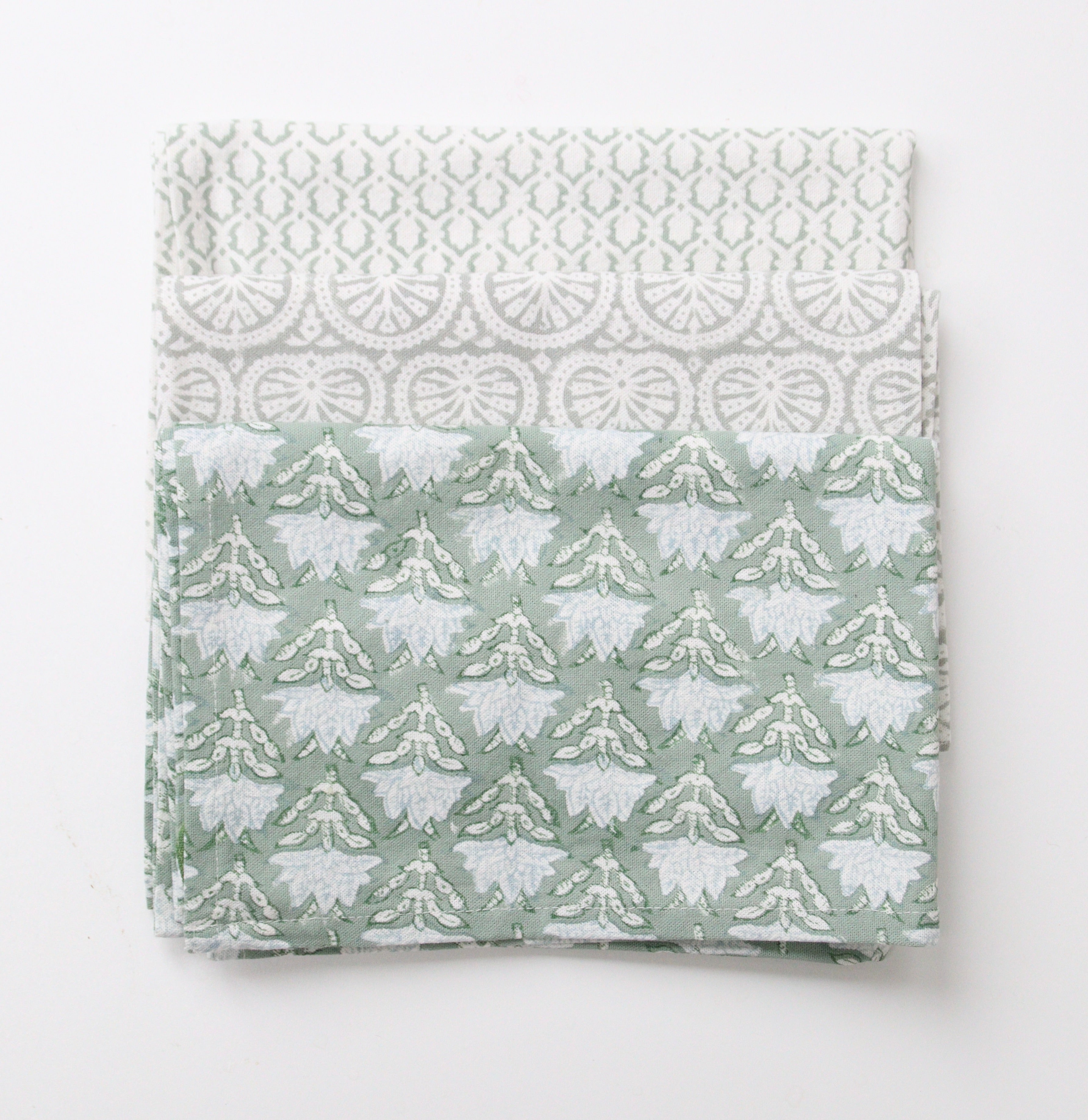 Drie theedoeken met verschillende prints in licht groen en zacht grijs liggen opgevouwen op elkaar. De bovenste heeft een print met bloemen, de middelste een print geïnspireerd op schelpen en de onderste een subtiele geometrisch print genaamd Little Crown. 